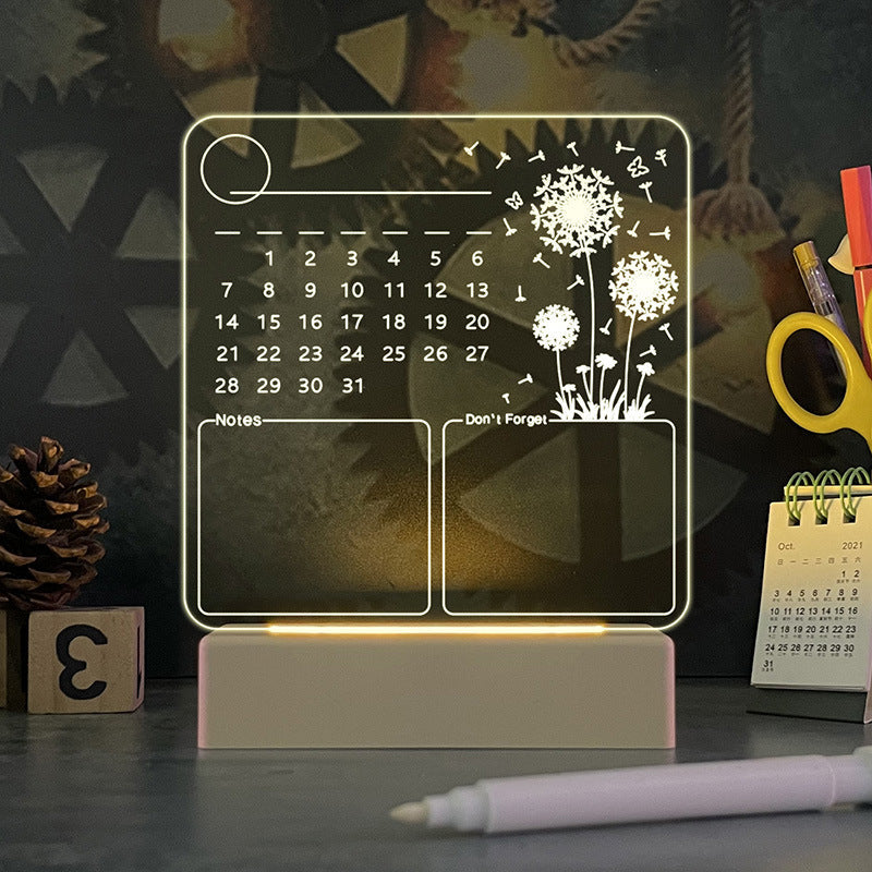 Acrylic calendar memo board with LED night light and dandelion design on desk with pen and USB base